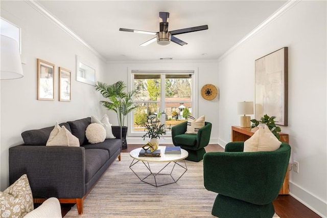 living room featuring a ceiling fan, crown molding, baseboards, and wood finished floors