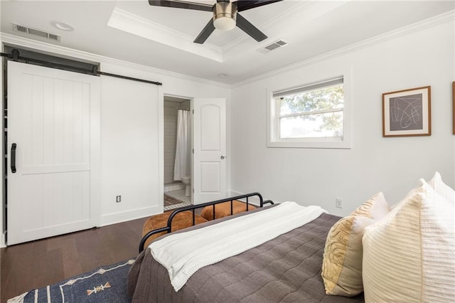 bedroom featuring a tray ceiling, a barn door, visible vents, and wood finished floors