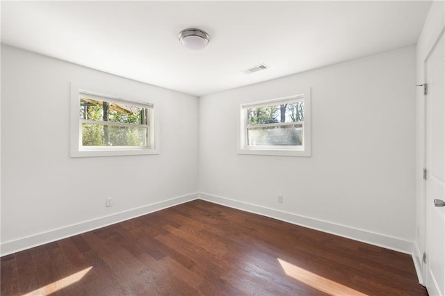 spare room featuring visible vents, baseboards, and dark wood-type flooring