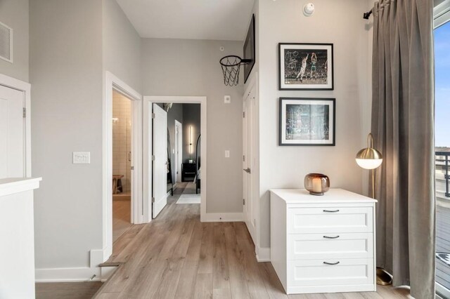 hall featuring visible vents, baseboards, and light wood finished floors