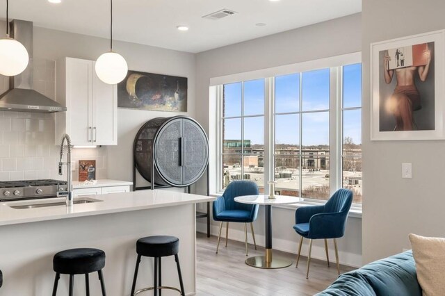 kitchen with visible vents, a breakfast bar, tasteful backsplash, white cabinetry, and wall chimney exhaust hood