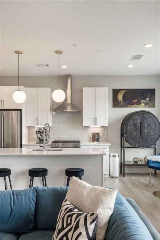 kitchen featuring light countertops, wall chimney range hood, backsplash, and freestanding refrigerator