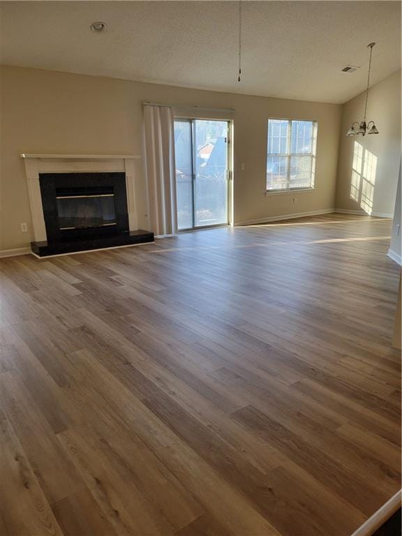 unfurnished living room with baseboards, a premium fireplace, wood finished floors, a notable chandelier, and a textured ceiling