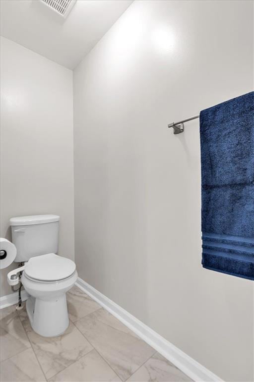 bathroom featuring toilet, visible vents, marble finish floor, and baseboards