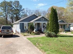 bungalow-style home with aphalt driveway, covered porch, and a front lawn