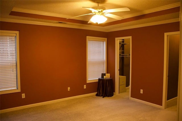 carpeted empty room featuring a tray ceiling, ornamental molding, and ceiling fan