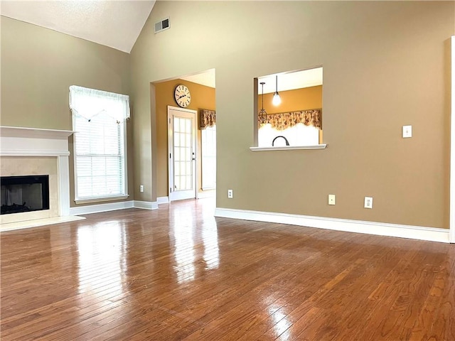 unfurnished living room with hardwood / wood-style flooring, high vaulted ceiling, and a premium fireplace