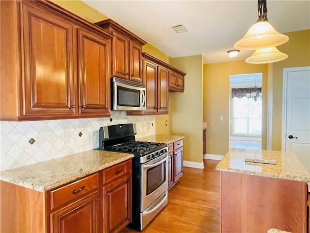 kitchen with light stone counters, hanging light fixtures, backsplash, and appliances with stainless steel finishes