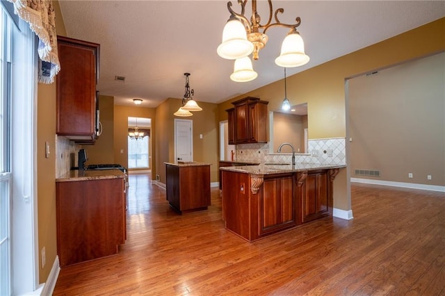 kitchen featuring pendant lighting, tasteful backsplash, wood-type flooring, kitchen peninsula, and an inviting chandelier