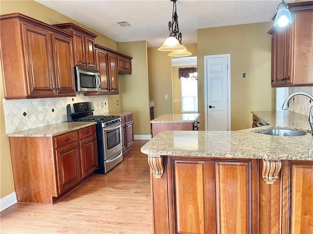 kitchen featuring appliances with stainless steel finishes, sink, hanging light fixtures, light stone counters, and light hardwood / wood-style flooring