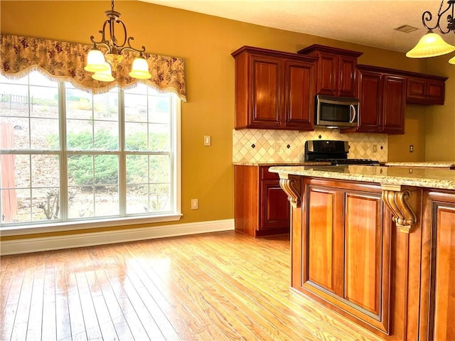 kitchen featuring decorative light fixtures, tasteful backsplash, range, light stone counters, and light hardwood / wood-style flooring