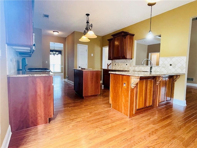 kitchen featuring hanging light fixtures, hardwood / wood-style flooring, backsplash, and kitchen peninsula