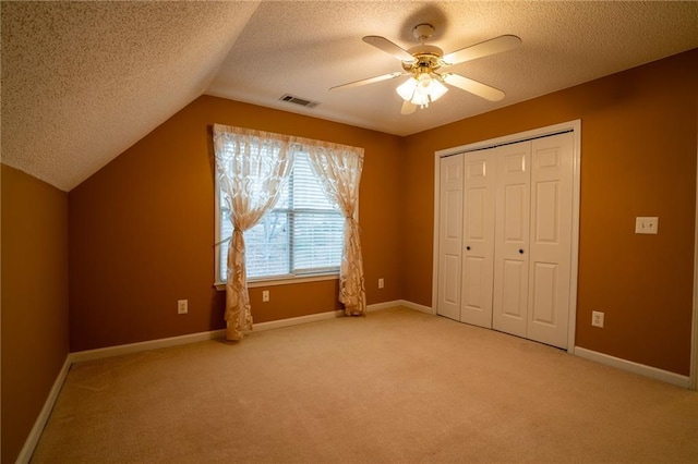 unfurnished bedroom featuring a closet, vaulted ceiling, carpet, and a textured ceiling