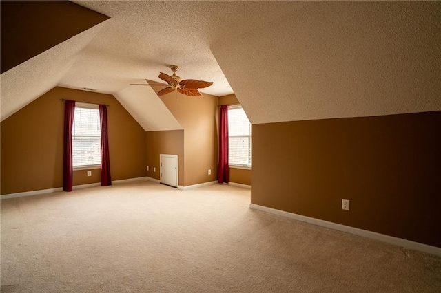 additional living space featuring light colored carpet, a healthy amount of sunlight, and a textured ceiling