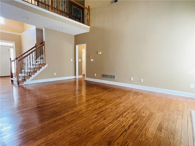 unfurnished living room with hardwood / wood-style flooring and a towering ceiling