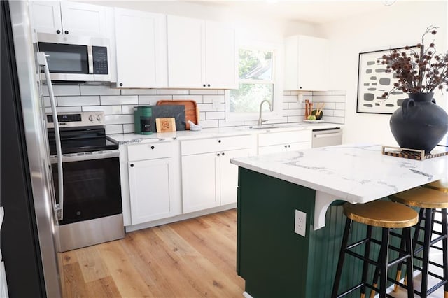 kitchen featuring light stone countertops, appliances with stainless steel finishes, sink, a kitchen island, and white cabinetry