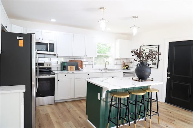 kitchen featuring hanging light fixtures, sink, a center island, white cabinetry, and appliances with stainless steel finishes