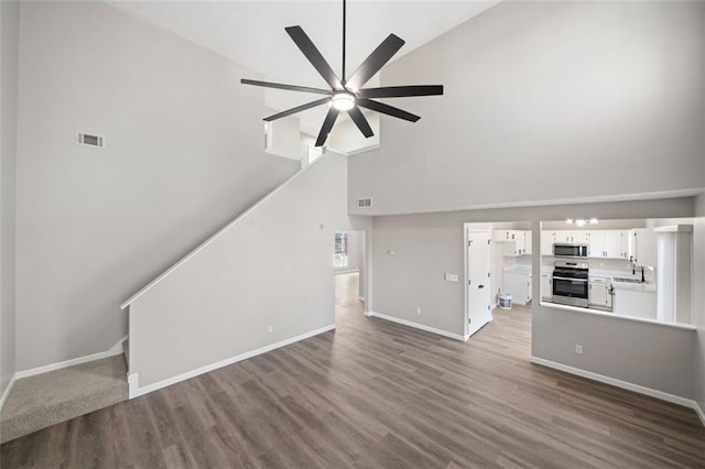 unfurnished living room featuring dark wood-type flooring, baseboards, visible vents, and high vaulted ceiling