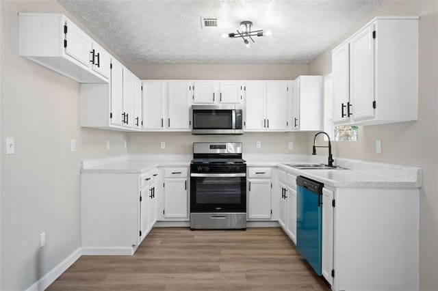 kitchen with stainless steel appliances, a sink, a textured ceiling, white cabinets, and light wood finished floors