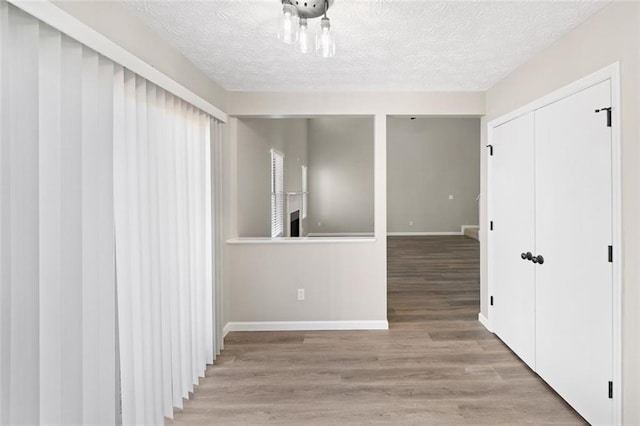 corridor featuring wood finished floors, baseboards, and a textured ceiling