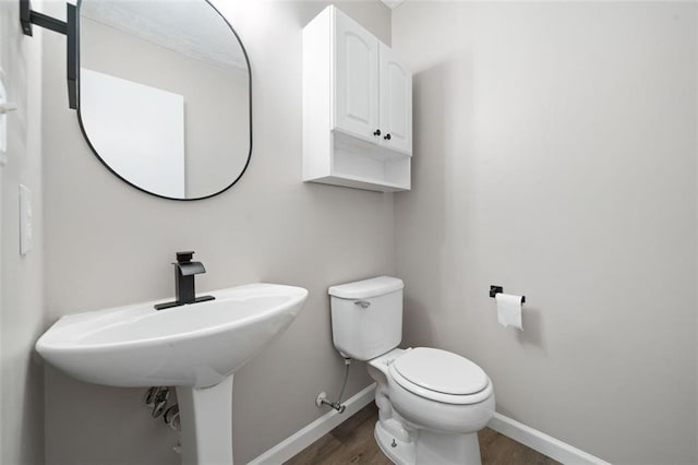 half bath with wood finished floors, baseboards, toilet, and a sink