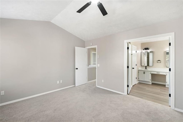 unfurnished bedroom featuring light colored carpet, lofted ceiling, baseboards, connected bathroom, and a ceiling fan