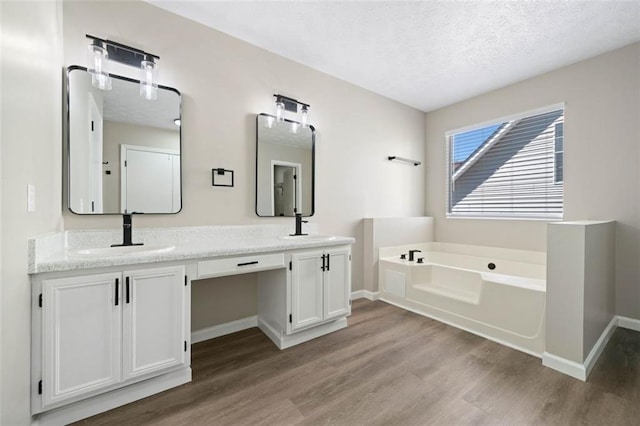 full bath featuring wood finished floors, a garden tub, a textured ceiling, baseboards, and double vanity