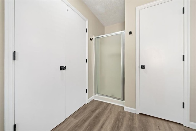 bathroom featuring wood finished floors, a shower stall, baseboards, and a textured ceiling