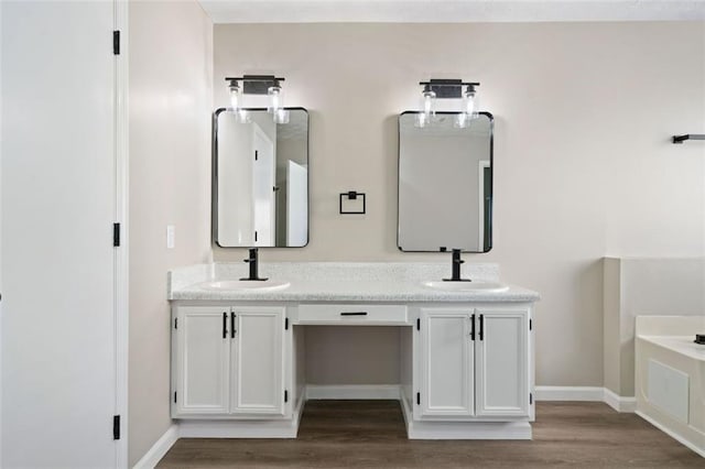 full bathroom featuring wood finished floors, double vanity, baseboards, and a bath