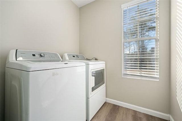 clothes washing area featuring separate washer and dryer, wood finished floors, baseboards, and healthy amount of natural light