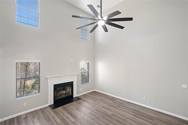 unfurnished living room featuring high vaulted ceiling, a glass covered fireplace, a ceiling fan, wood finished floors, and baseboards