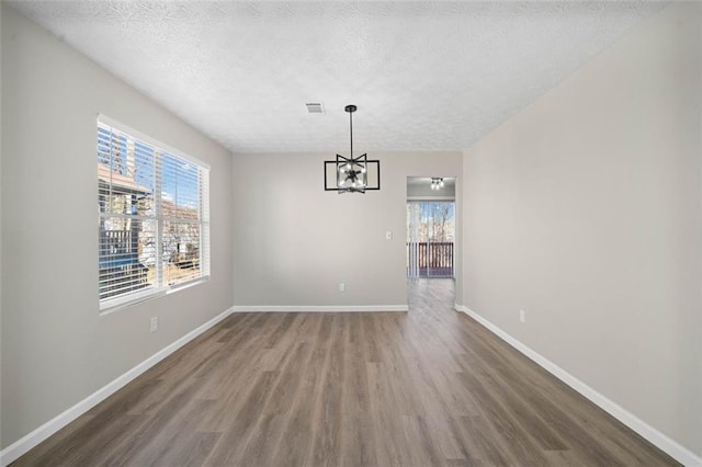 unfurnished dining area with wood finished floors, plenty of natural light, a chandelier, a textured ceiling, and baseboards