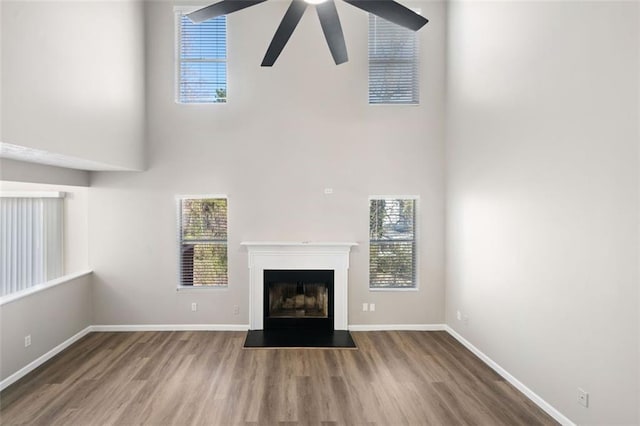 unfurnished living room featuring a glass covered fireplace, a healthy amount of sunlight, baseboards, and wood finished floors