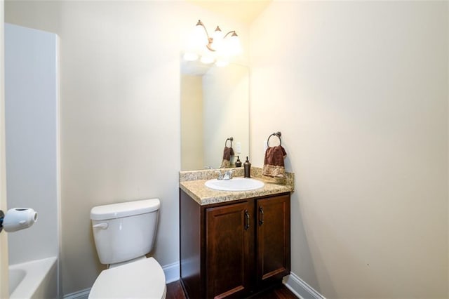 bathroom with a bathtub, toilet, vanity, and baseboards