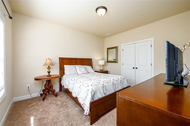 bedroom with a closet, light colored carpet, and baseboards