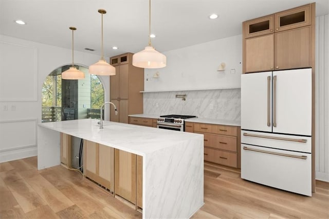 kitchen featuring sink, white fridge, light hardwood / wood-style floors, an island with sink, and stainless steel range with gas stovetop