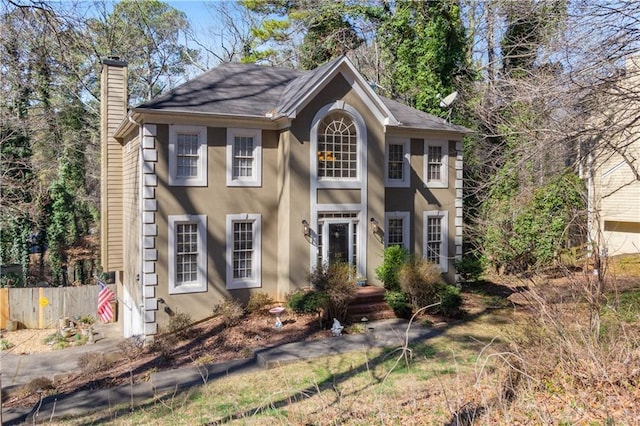 colonial house featuring a chimney, fence, and stucco siding