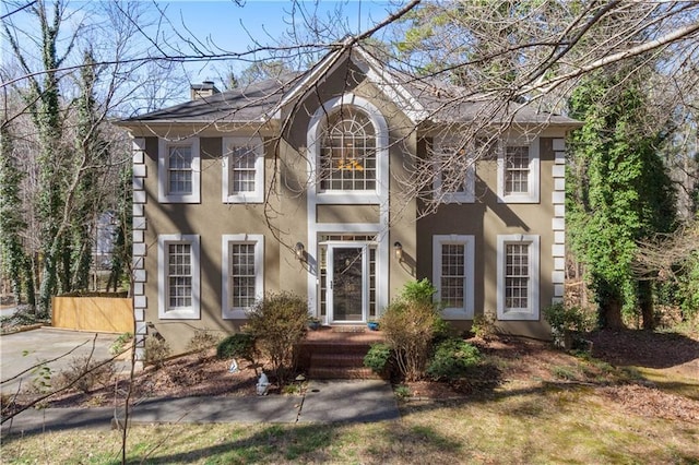 colonial inspired home with a chimney and stucco siding