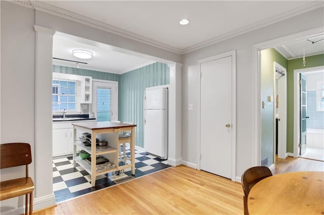 kitchen with crown molding, freestanding refrigerator, light wood-style flooring, a sink, and baseboards