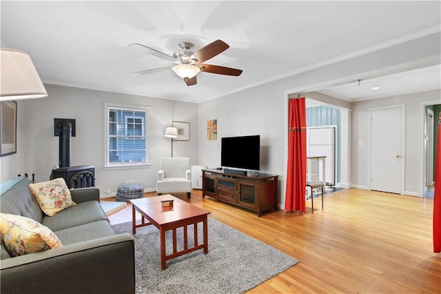 living area with baseboards, ornamental molding, light wood-style flooring, a ceiling fan, and a wood stove