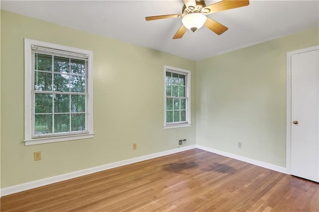 empty room with visible vents, a wealth of natural light, wood finished floors, and baseboards