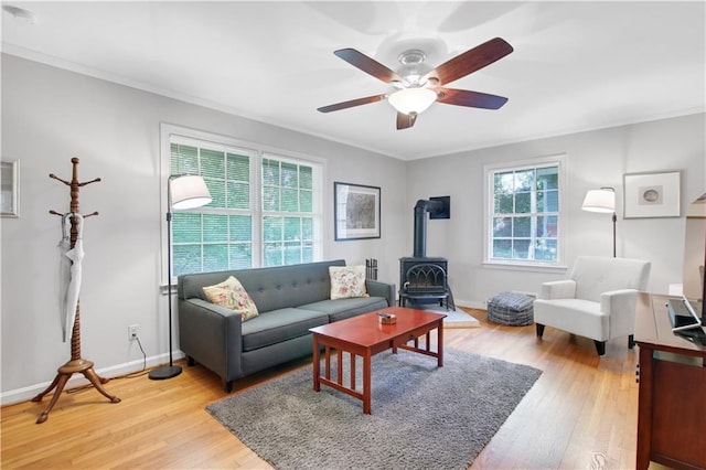 living area with light wood finished floors, a wood stove, ceiling fan, and ornamental molding