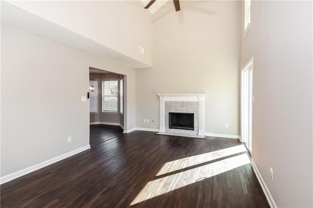 unfurnished living room featuring a fireplace, ceiling fan, a towering ceiling, and dark wood-type flooring