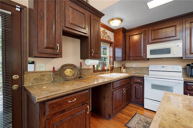 kitchen with dark brown cabinets, white appliances, sink, and light hardwood / wood-style flooring