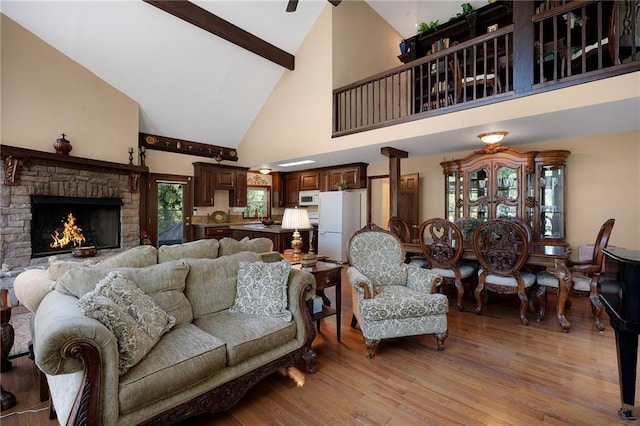 living room with beamed ceiling, light wood-type flooring, high vaulted ceiling, and a stone fireplace