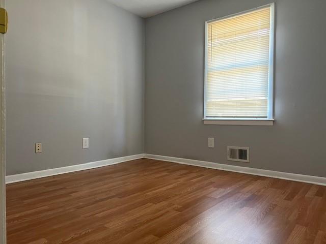 unfurnished room featuring baseboards, visible vents, plenty of natural light, and wood finished floors