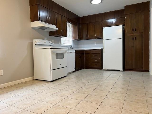 kitchen with dark brown cabinets, white appliances, baseboards, light countertops, and under cabinet range hood
