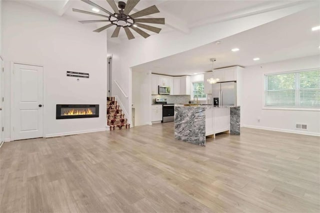 unfurnished living room featuring ceiling fan, vaulted ceiling with beams, light hardwood / wood-style flooring, and sink