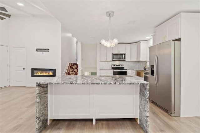 kitchen with light wood-type flooring, light stone counters, white cabinetry, appliances with stainless steel finishes, and decorative light fixtures