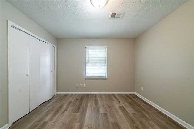 unfurnished bedroom with baseboards, a textured ceiling, wood finished floors, and a closet